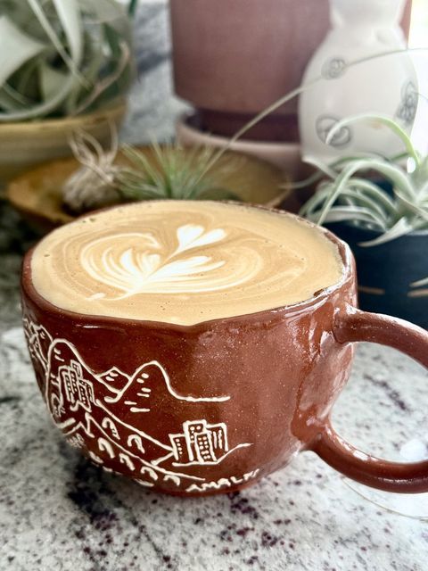 Latte art in a red clay mug carved with an Amalfi coast scene
