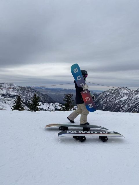 Kay carrying a snowboard at the top of a mountain run