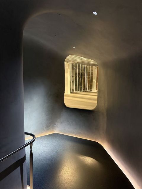 A softly lit curved tunnel with a window looking into a bright hall